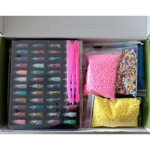 Toy slime in various colours in plastic pots with plastic lids. The set also includes bottles of glitter in a variety of colours, as well as small colourful balls and pink mixing tools.