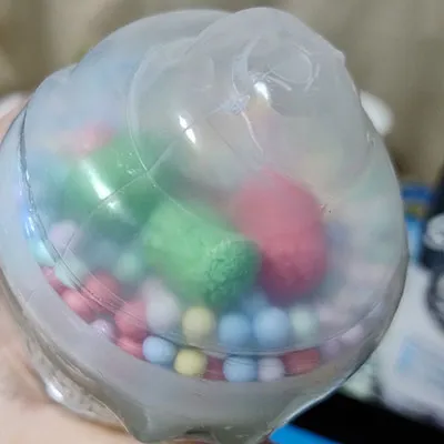 Yellow slime with small coloured balls and three larger coloured rollers in the plastic lid of the toy.