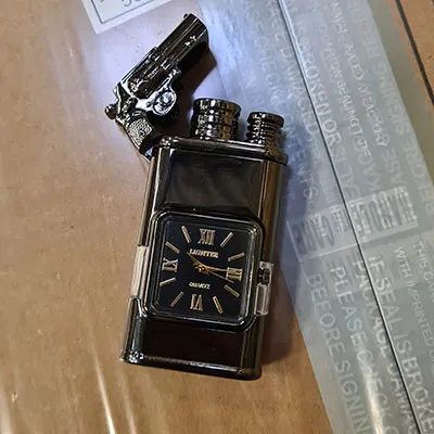 Metal lighter with a built-in clock. On top of the lighter there is small gun attached.
