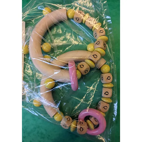 Wooden rattle toy with yellow beads, a pink ring and the letters of the name marked on the cubes.