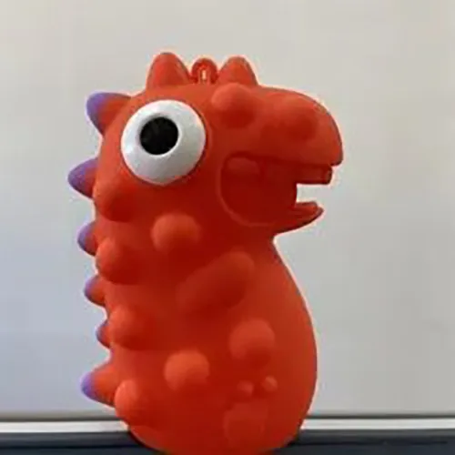 Soft red plastic dinosaur toy, containing an LED, with a purple crest and black and white eyes which stick out from the head when the toy is squeezed.