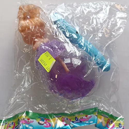 Plastic doll in a purple textile dress. The doll's legs are placed in a transparent plastic ball with feathers. A controller, including a battery, is attached to the doll’s head.
