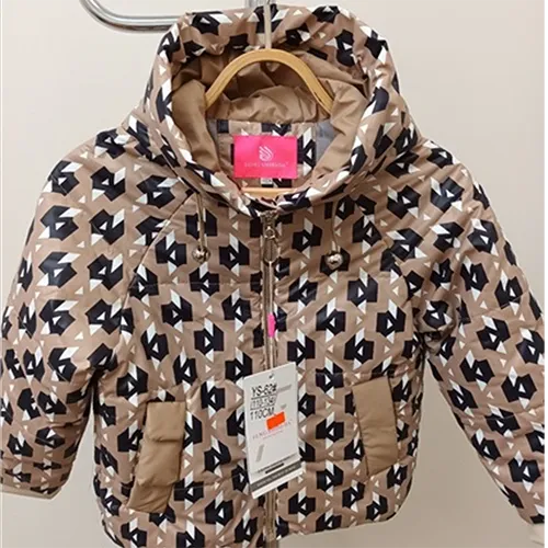 Jacket intended for young children, with a top made of cream-coloured textile fabric quilted with horizontal stripes, printed with regular black and white figures. The hood uses a functional elastic drawstring in the form of a loop, the ends of the loops protrude freely by about 7 cm.