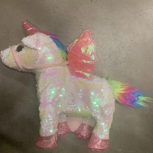 Battery-powered toy unicorn with a textile surface with white/pink shiny reversible scales, The colour of the scales changes with touch.The unicorn's horn is pink, shiny and it has a pink strap on the muzzle, a rainbow-coloured mane and tail, pink wings attached to the back, and pink shoes on the bottom of the legs. It also has a decorative element with a heart-shaped h