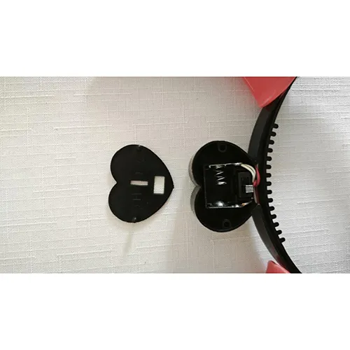 Glowing toy plastic headband in the shape of devil horns, battery-operated. In the middle of the headband there is a heart-shaped cover for two AG13 batteries.