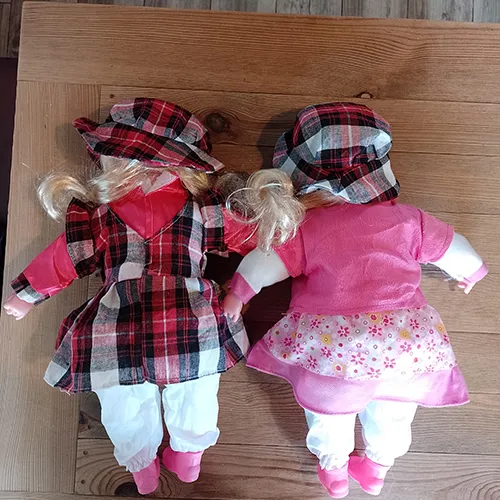 Textile doll with a plastic head, hands and shoes. The doll has long blonde hair and is dressed in a coloured dress and underpants. Under the dress, there is a removable battery compartment for three pieces of LR44 batteries.