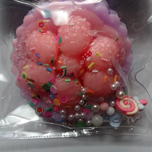 Anti-stress toy, 10cm long, made of purple-pink soft plastic confectionery (tartlet with berries) with multi-coloured plastic sprinkles, coloured/pearl balls of various sizes, with plastic candies (2 cm) and a flower (1.5 cm).