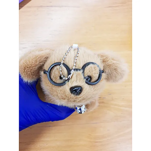 Plush toy, in the shape of a brown puppy with black glasses and a collar with a bell. Product sold online, in particular via Shein.