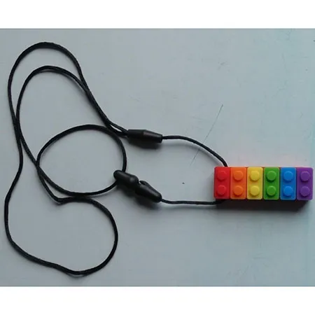 Teether in the shape of a toy construction brick with a cord and detachable parts. Product sold online, in particular via eBay (unique identifer: 167636875338).