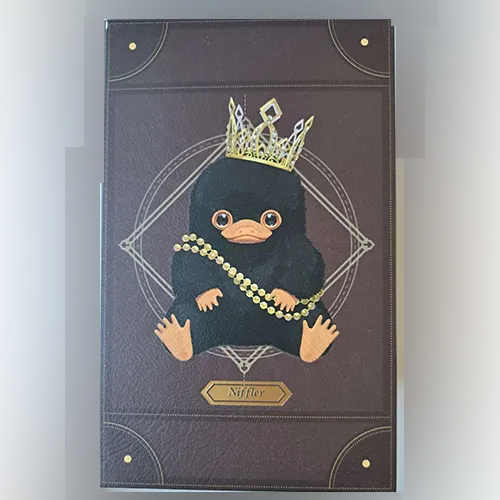 Soft toy, in the shape of a Niffler creature, with a gold-finish crown and a beaded necklace. Product sold online, in particular via Shein.