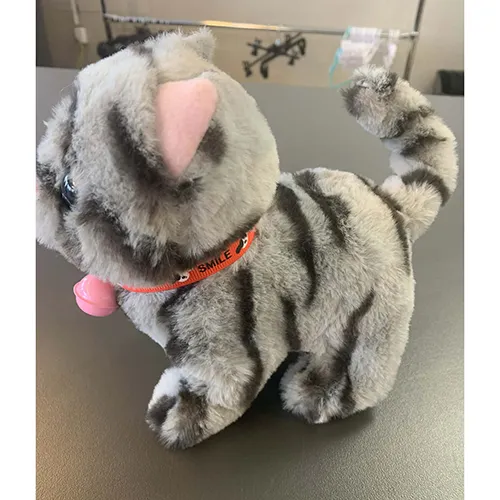 Plastic toy in the shape of a grey striped cat with blue eyes, a pink nose, a bright orange collar with the inscription