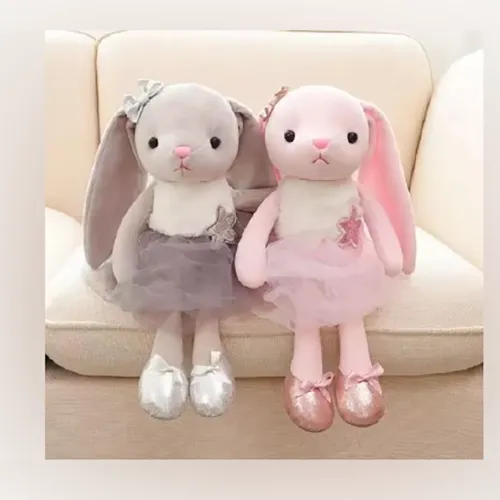 Soft toy, in the shape of a pink rabbit with long green and pink ears, wearing a pink dress.