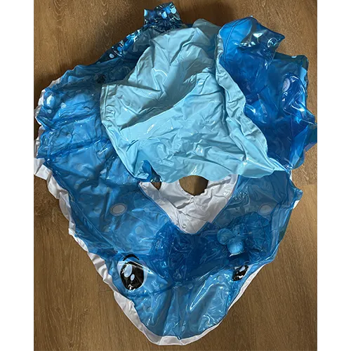 Blue inflatable swim seat with canopy, in the shape of a fish with a roof structure. Several balls with bells are integrated into the front area above the fish’s head.