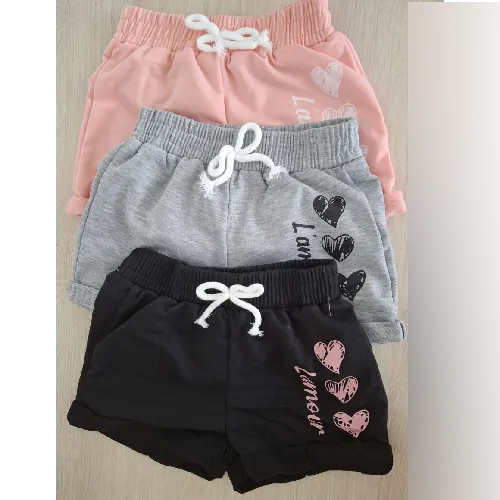 Set of three pairs of shorts intended for children, in different colours (grey, pink, and black), featuring a printed design on the left thigh, as well as a decorative bow made from a white drawstring attached with a stitch at the waist. Stated composition: 95% polyester, 5% elastane.