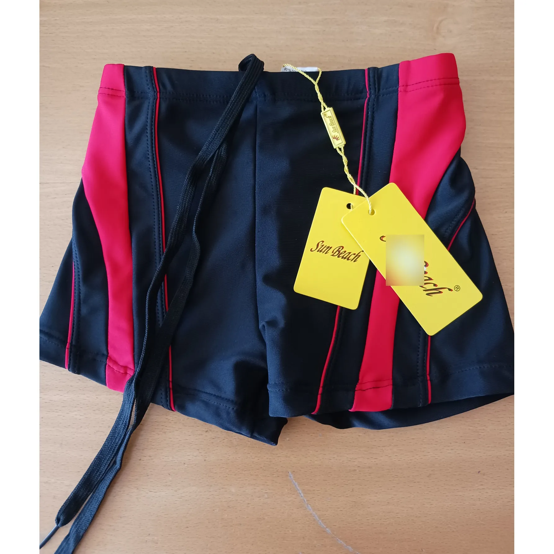 Swim briefs made of black and red knit fabric. It bears a textile drawstring with loose ends at the waistband.